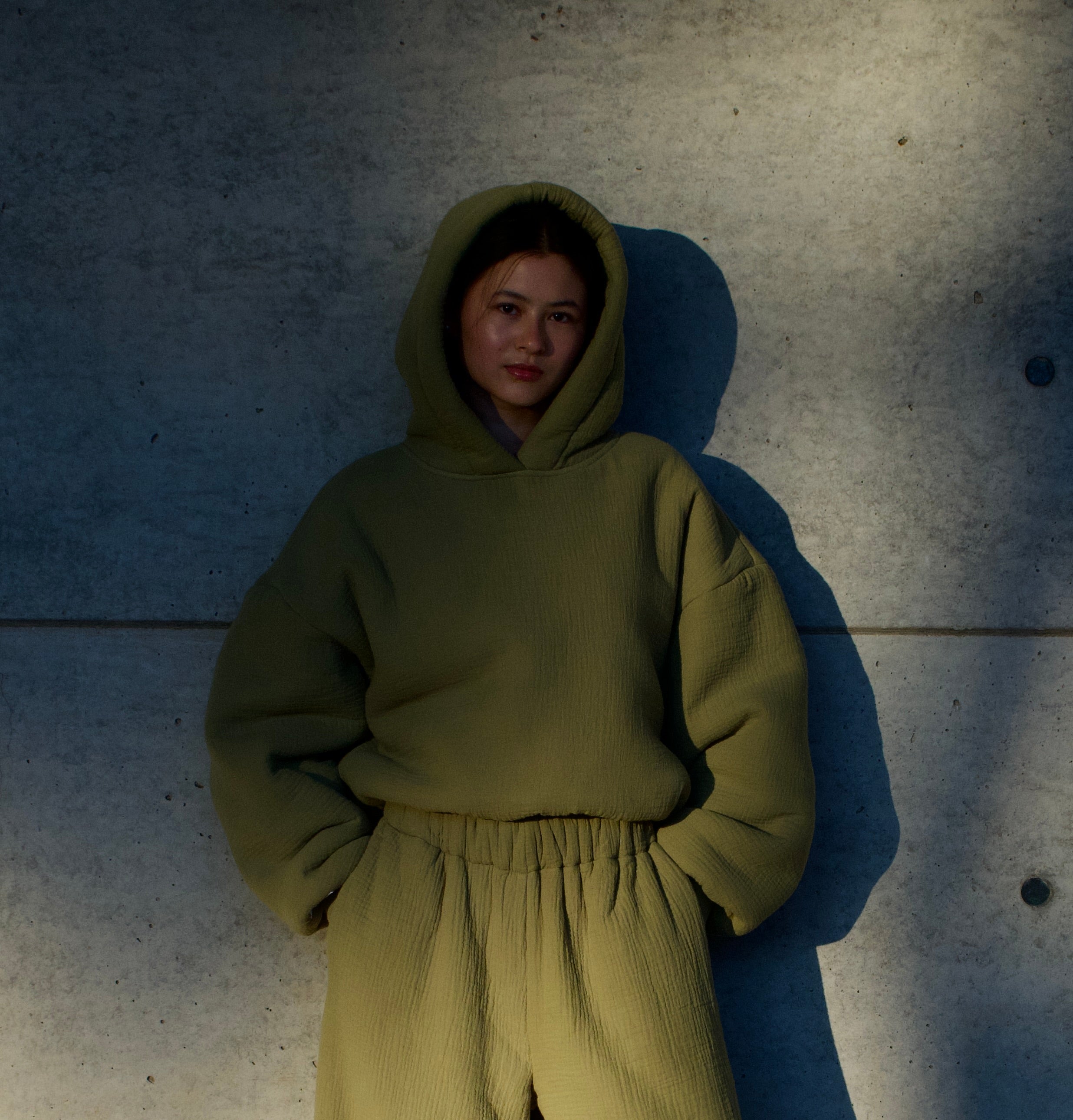 Person wearing a matcha green hoodie and pants against a textured wall.