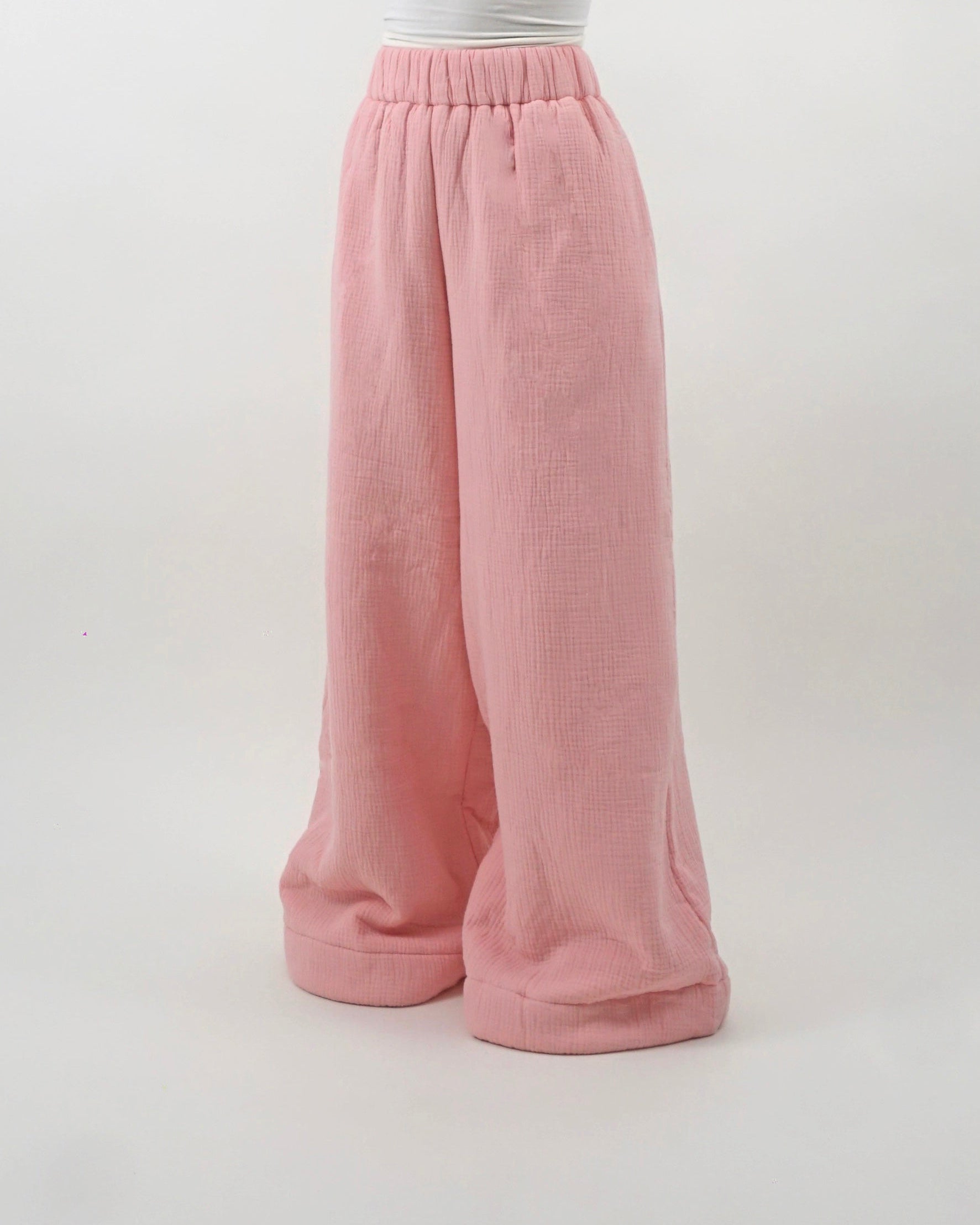 Pink wide-leg pants worn over a white top on a light gray background