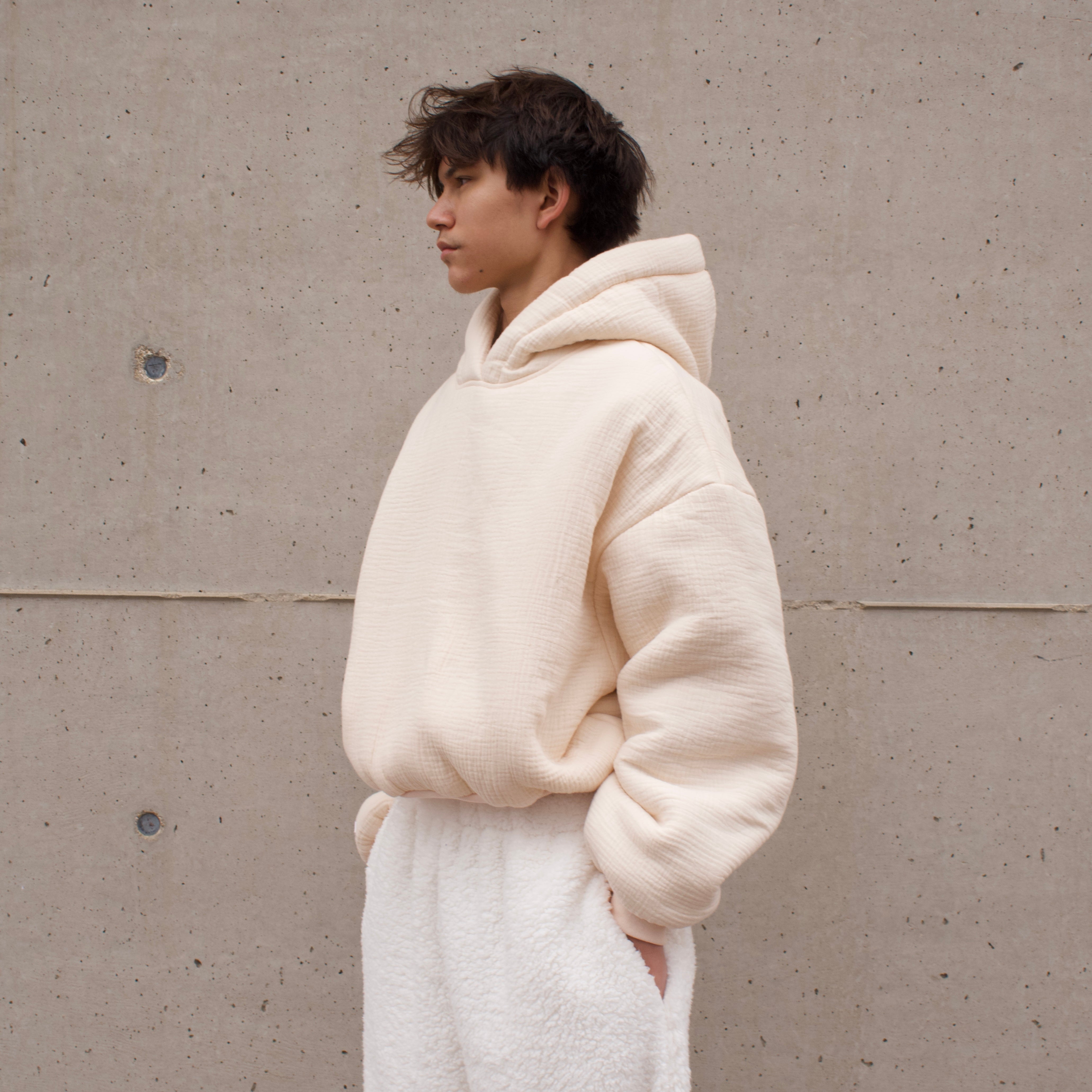 Person wearing a beige hoodie and full sherpa pants against a plain wall